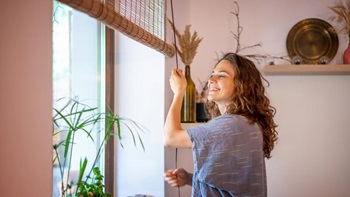 Mulher em casa com ar satisfeito baixa as persianas